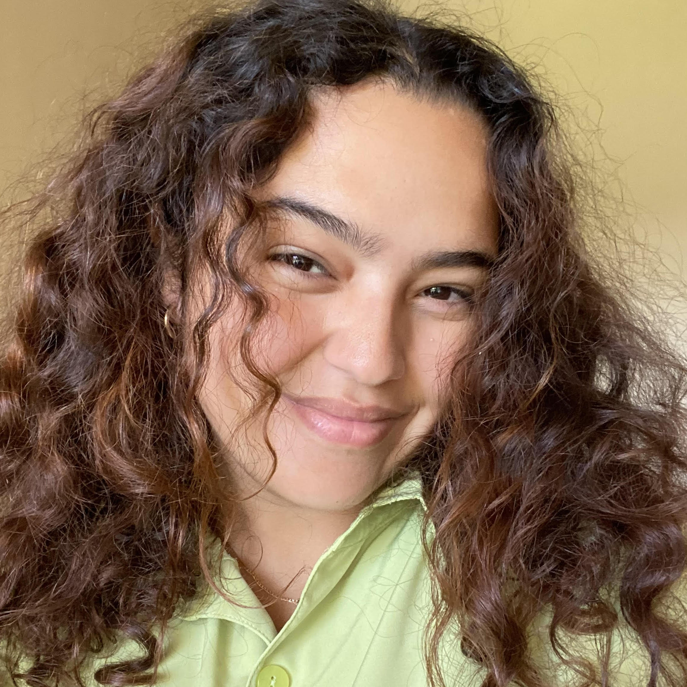 Israa - A woman with curly hair smiling in a green shirt.