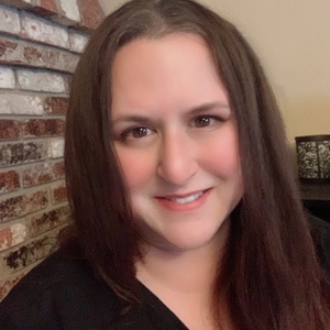 A woman smiling in front of a fireplace.